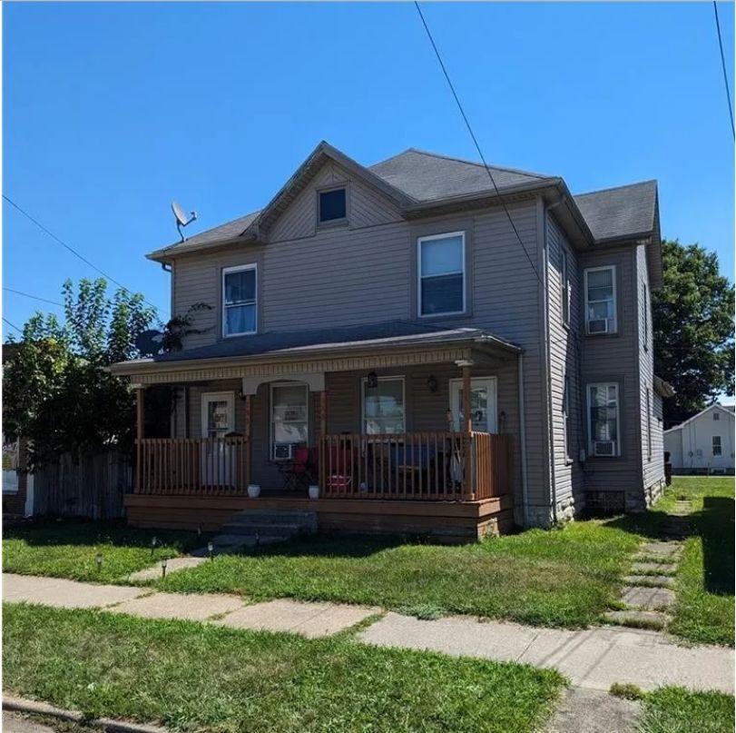 Two-story gray house with a covered front porch and trimmed lawn, under a clear blue sky.